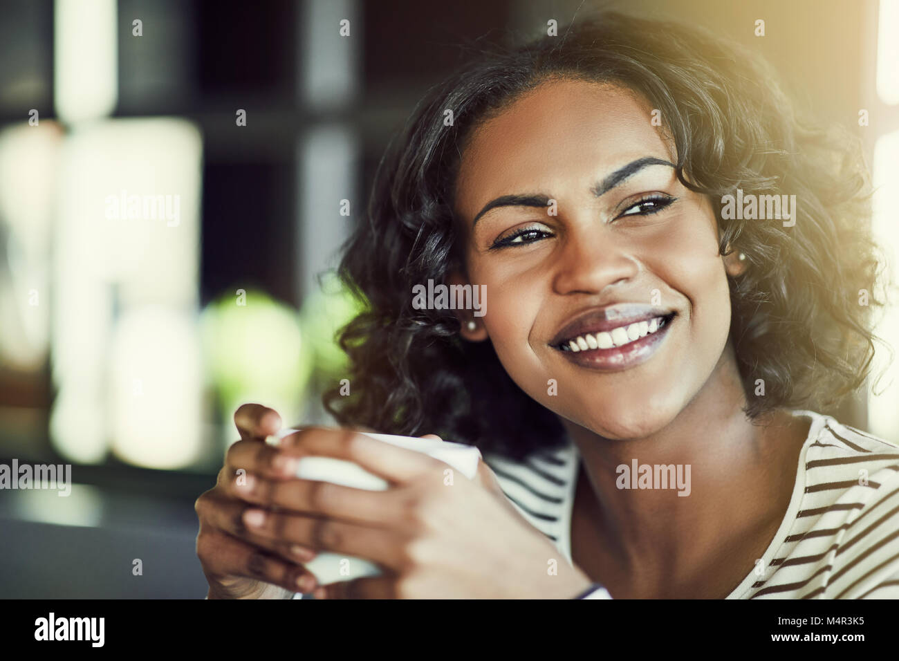 Young African woman smiling while sitting alone at a cafe table ...