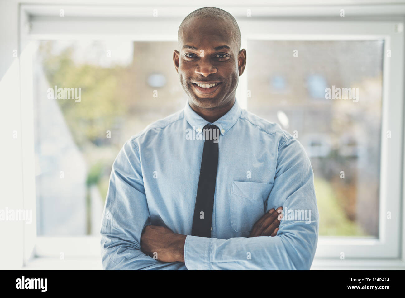 Smiling African businessman wearing a shirt and tie standing confidently with his arms crossed in his home office Stock Photo