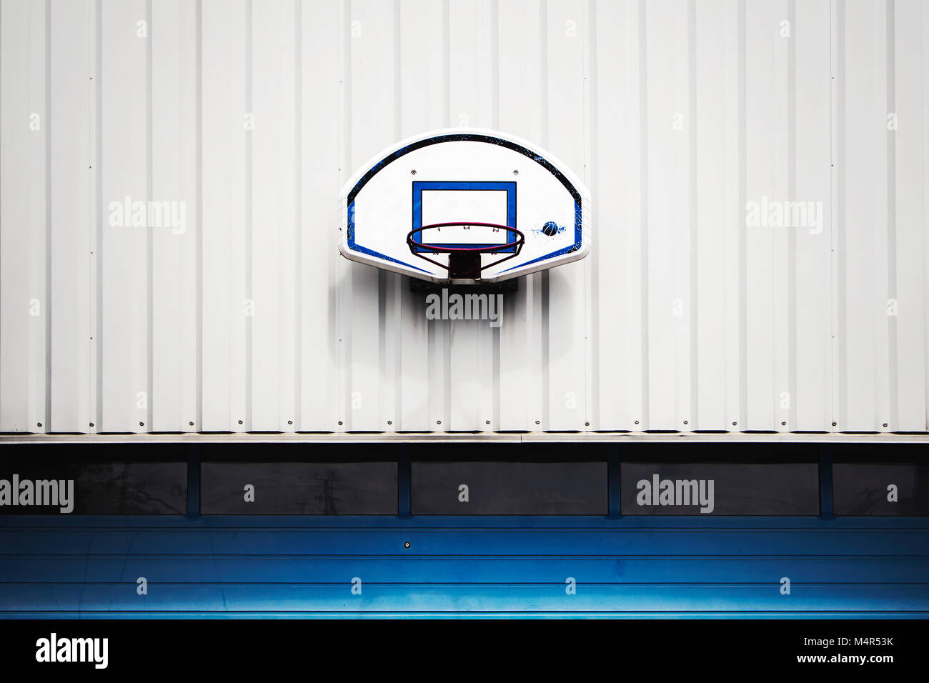 Basketball hoop fixed on a white wall above the blue garage door. Stock Photo
