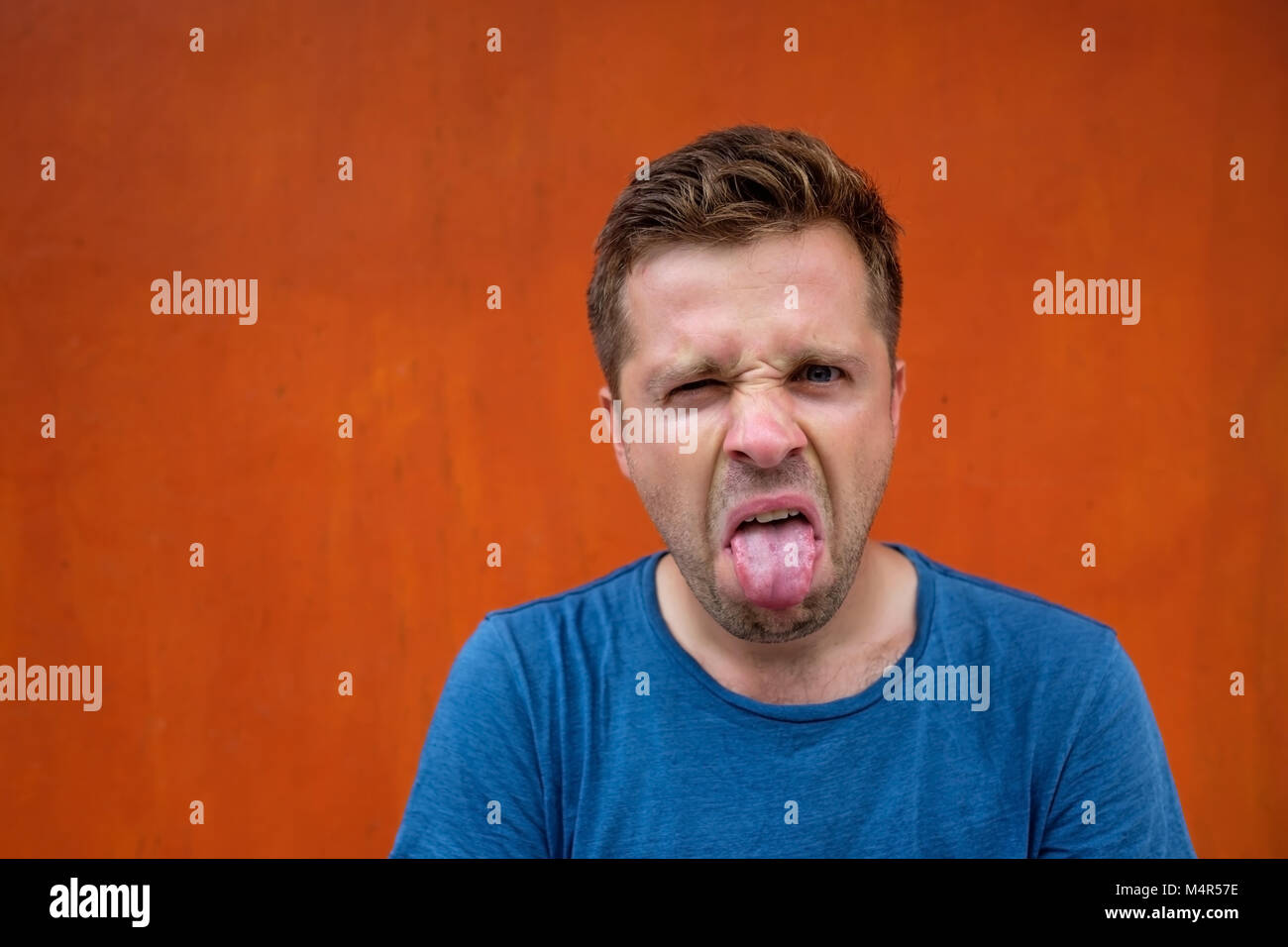 A young man with a grimace of disgust on his face. He puts out his tongue. Stock Photo