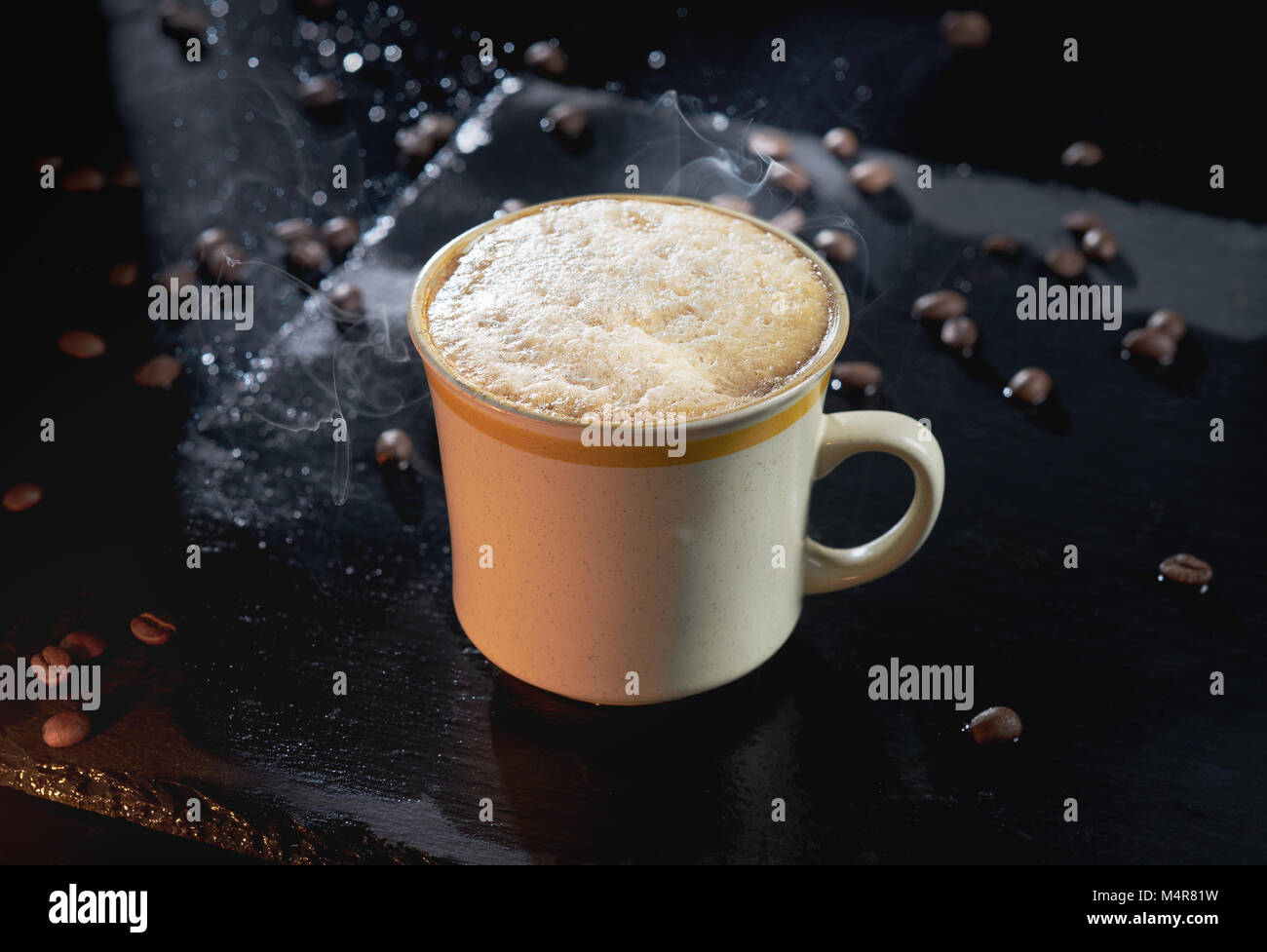 Piping hot coffee with white foam and steam surrounded by coffee beans Stock Photo