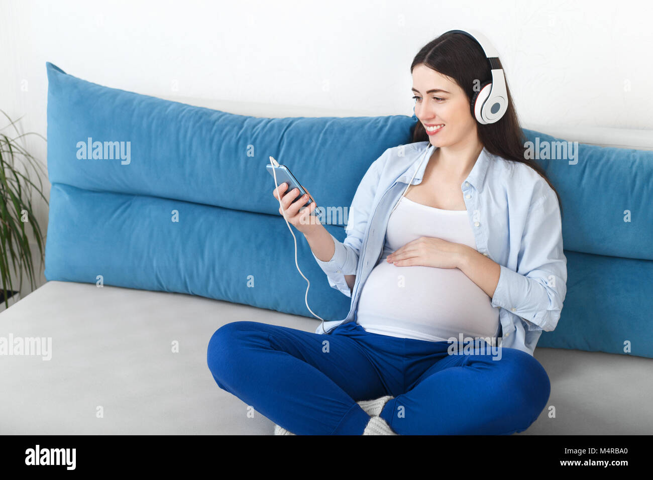 happy pregnant woman listening music in headphones and touching her belly. Pregnancy, people, technology concept Stock Photo