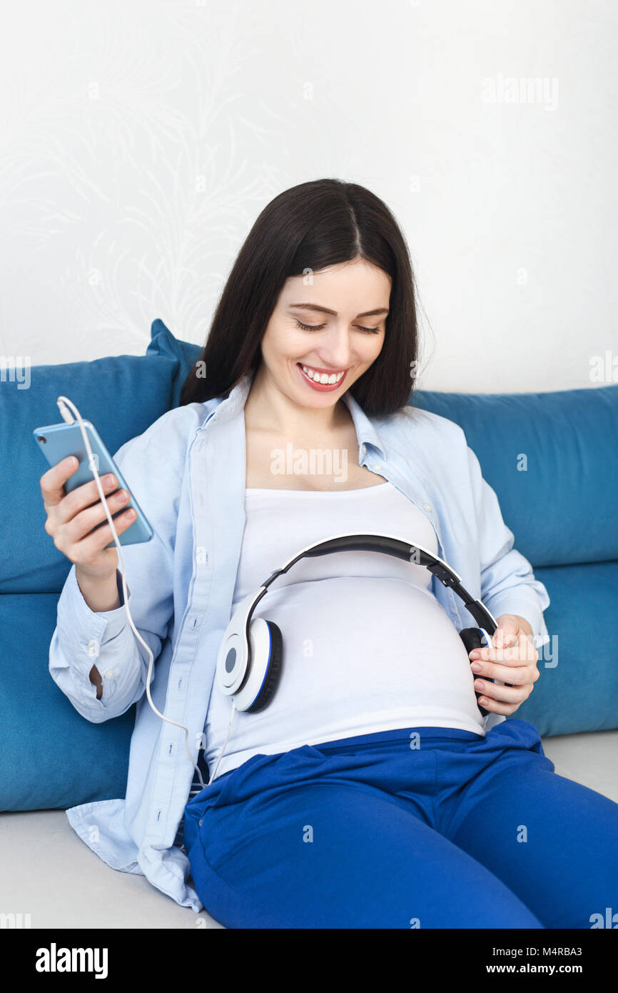 happy pregnant woman holding headphones on her belly at home. Pregnancy, people, technology concept Stock Photo