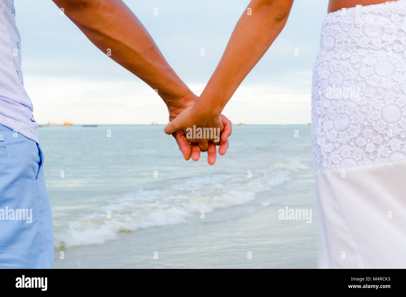 Couple holding hands having the sea as a background. View of the arms in the center and part of the bodies in the sides. Stock Photo