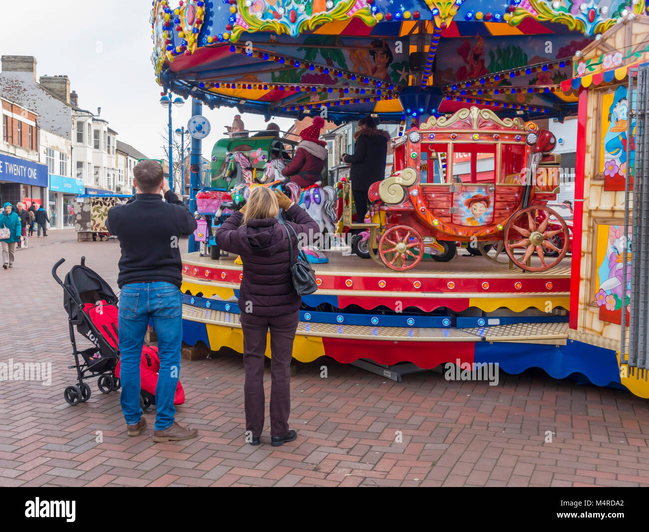 Parents photographing their children riding on a roundabout  set up in Redcar High Street Stock Photo