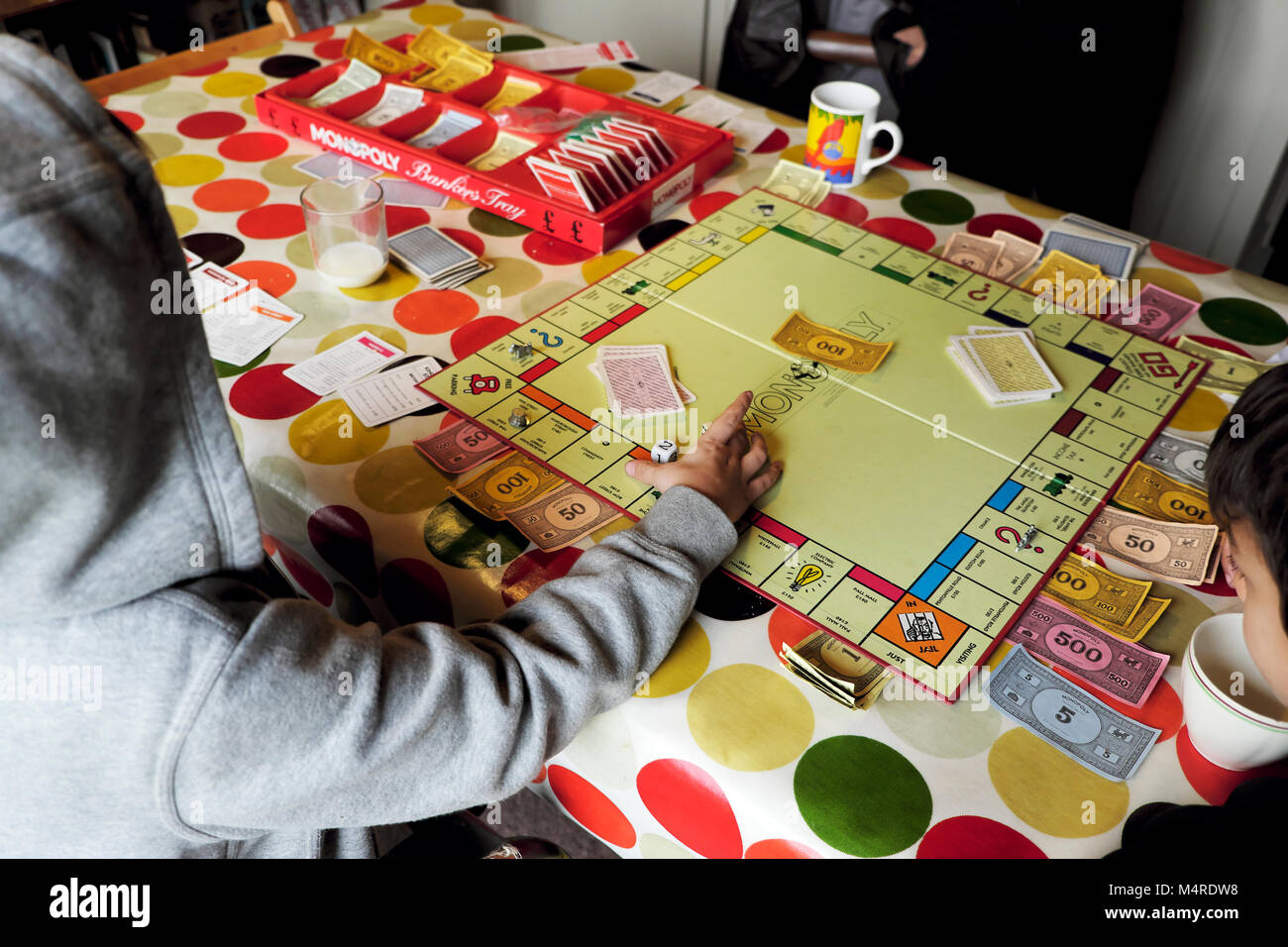 Monopoly board game being played by children friends inside a house on a table with colourful tablecloth at half-term in Carmarthenshire Wales UK Stock Photo