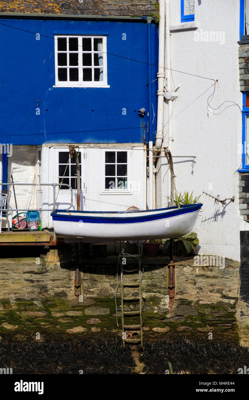 Blue and white dinghy on davits contrasts with the painted house walls at the harbourside in Polperro, Cornwall, UK Stock Photo