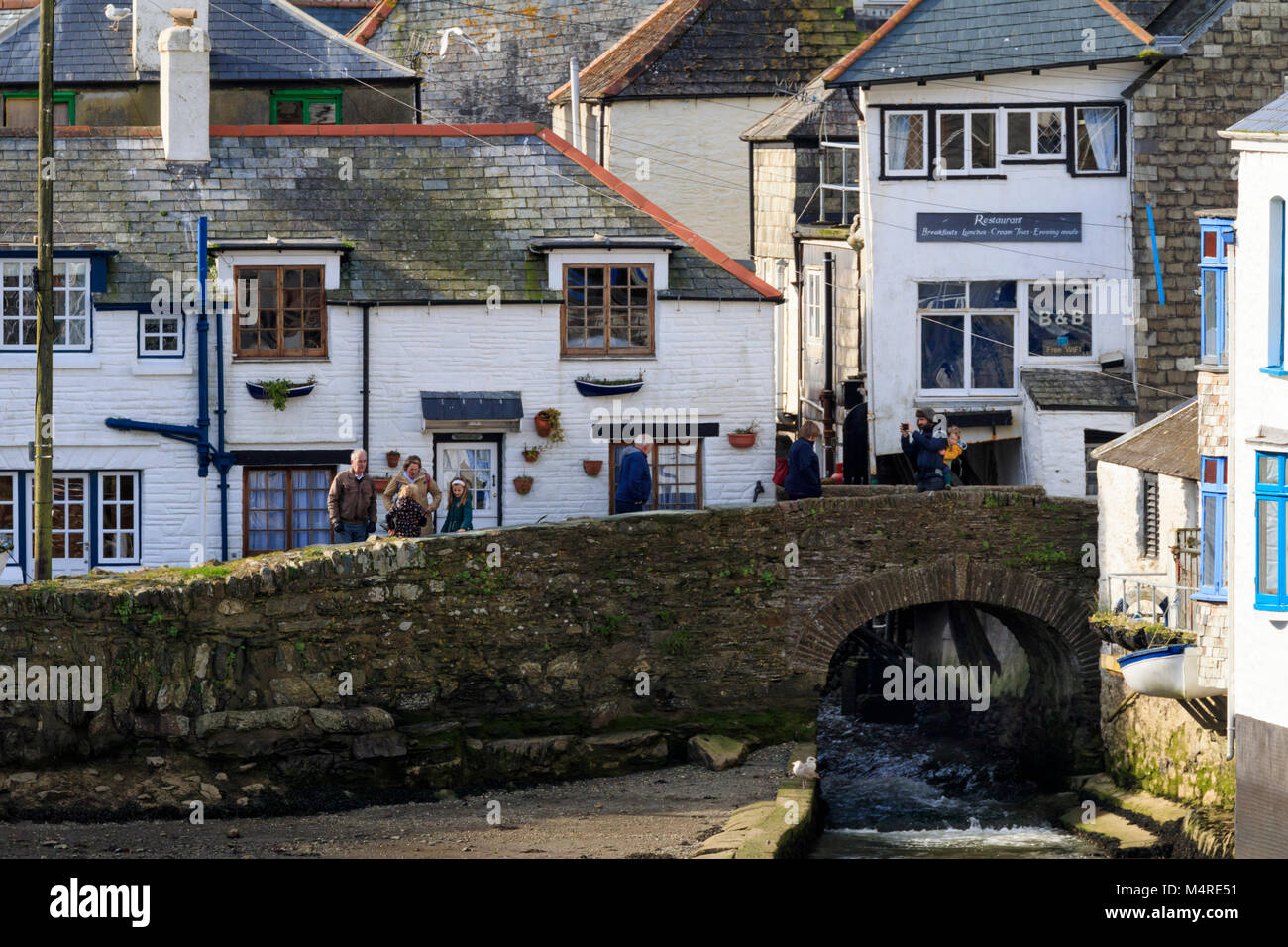 Winter visitors on the old stone bridge over the River Pol at the end of the harbour at Polperro, Cornwall, Uk Stock Photo