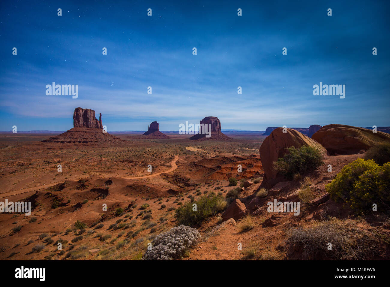 Classic panoramic view of scenic Monument Valley with the famous Mittens and Merrick Butte illuminated in beautiful mystic moonlight on a starry night Stock Photo