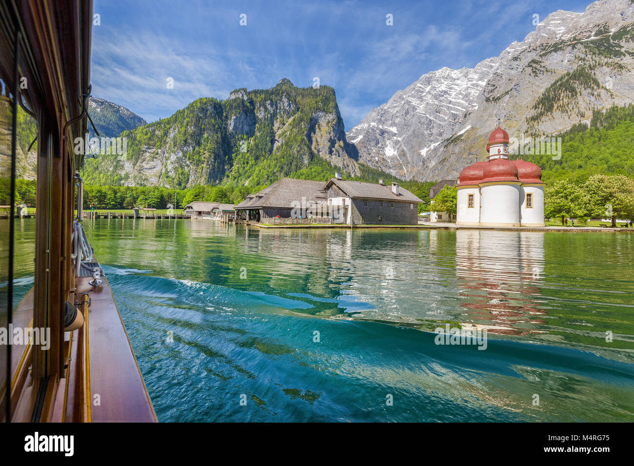 Classic view of traditional passenger boat gliding on Lake Konigssee with world famous Sankt Bartholomae pilgrimage church and Watzmann mountain Stock Photo