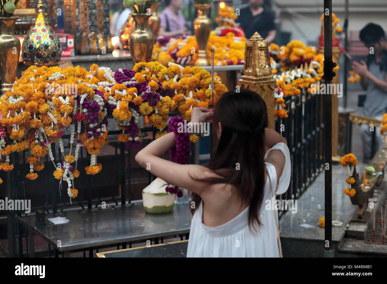 A young woman is praying and making incense offerings in the buddhist temple of Rachaprasong in