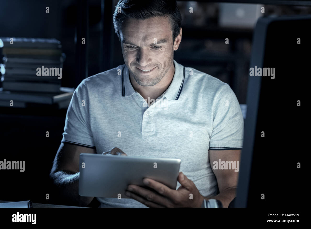 Joyful millennial man smiling while working on touchpad Stock Photo
