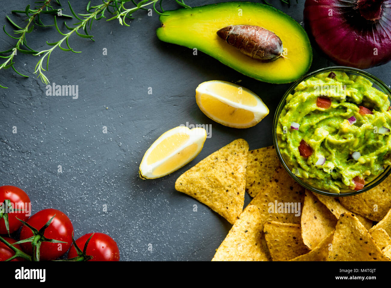 Guacamole bowl with ingredients and tortilla chips on a stone table. Top view image. Copyspace for your text. Stock Photo