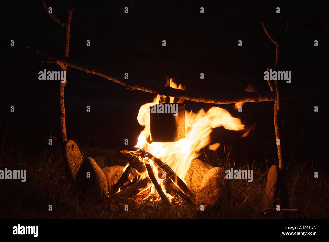 Cooking meal in a kettle on burning campfire in wild camping at night ...