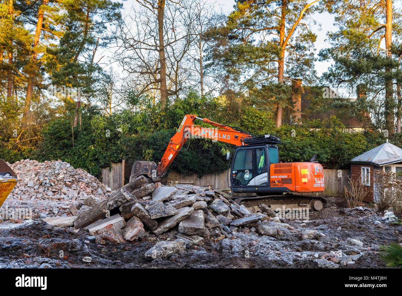 Construction site with orange heavy plant tracked mechanical excavator: remains of the demolition of a residential house prior to redevelopment Stock Photo
