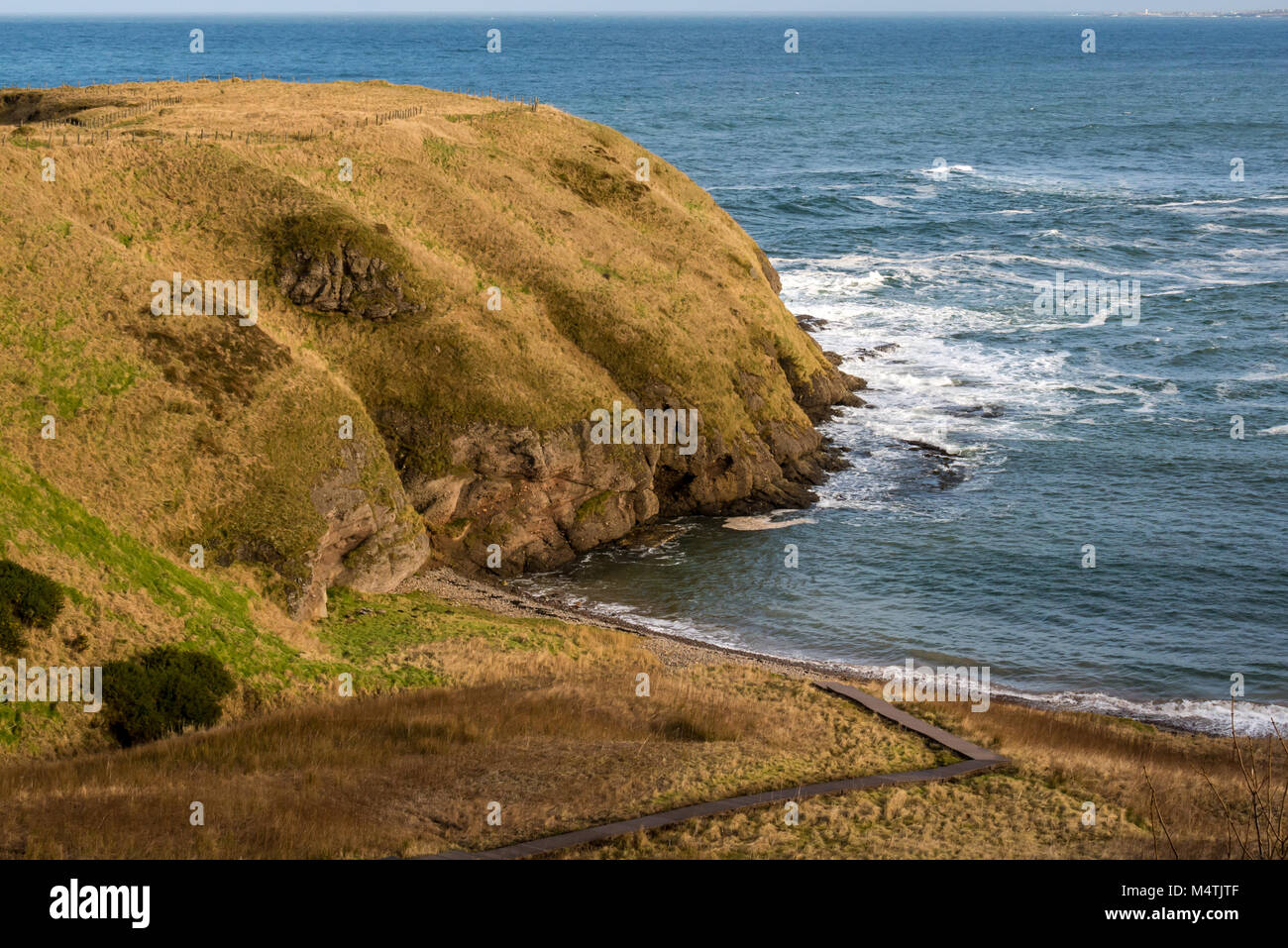 Looking down to small pebble beach cove, Cullykhan Bay, Aberdeenshire, Scotland, UK, and promontory of ancient vitrified Fort Fiddes Stock Photo