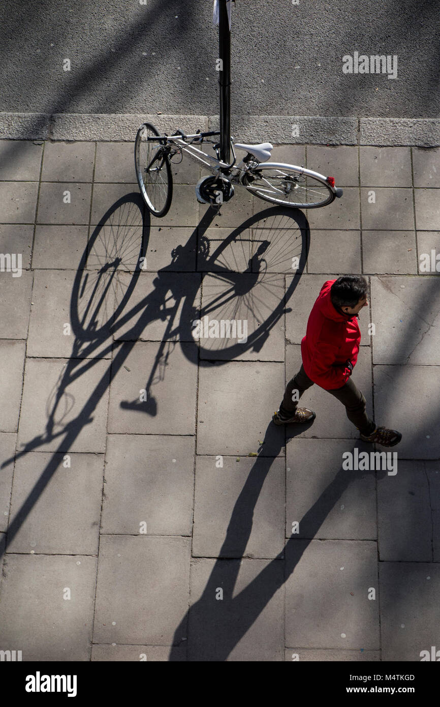 An unusual view of a pedestrian passing a parked bike with long shadows on the pavement Stock Photo