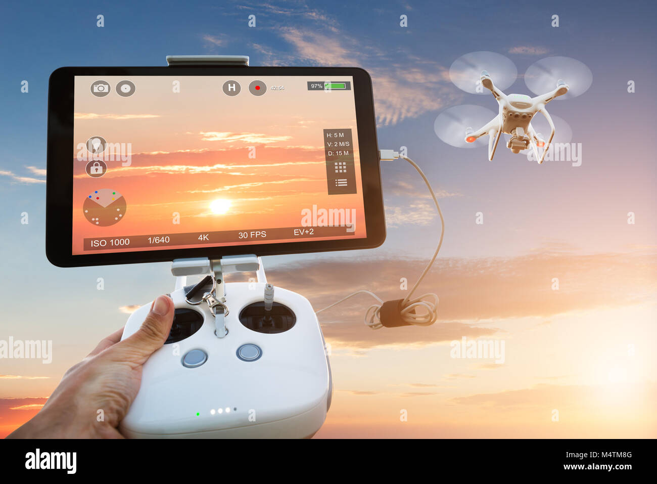 Cropped image of hand controlling drone filming orange sky seen on