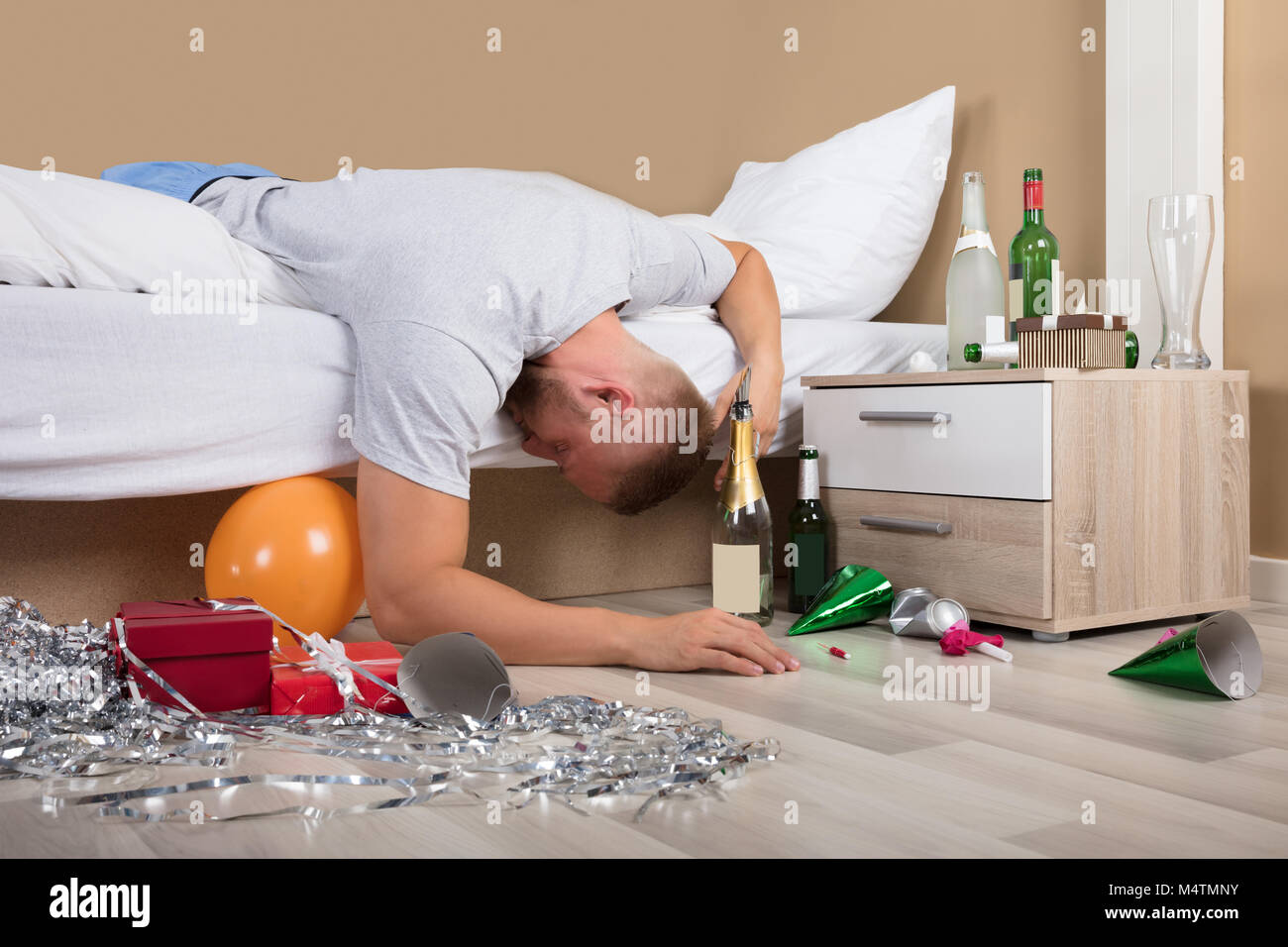 Young Man Lying On Bed With Messed Up Floor After Party Stock Photo