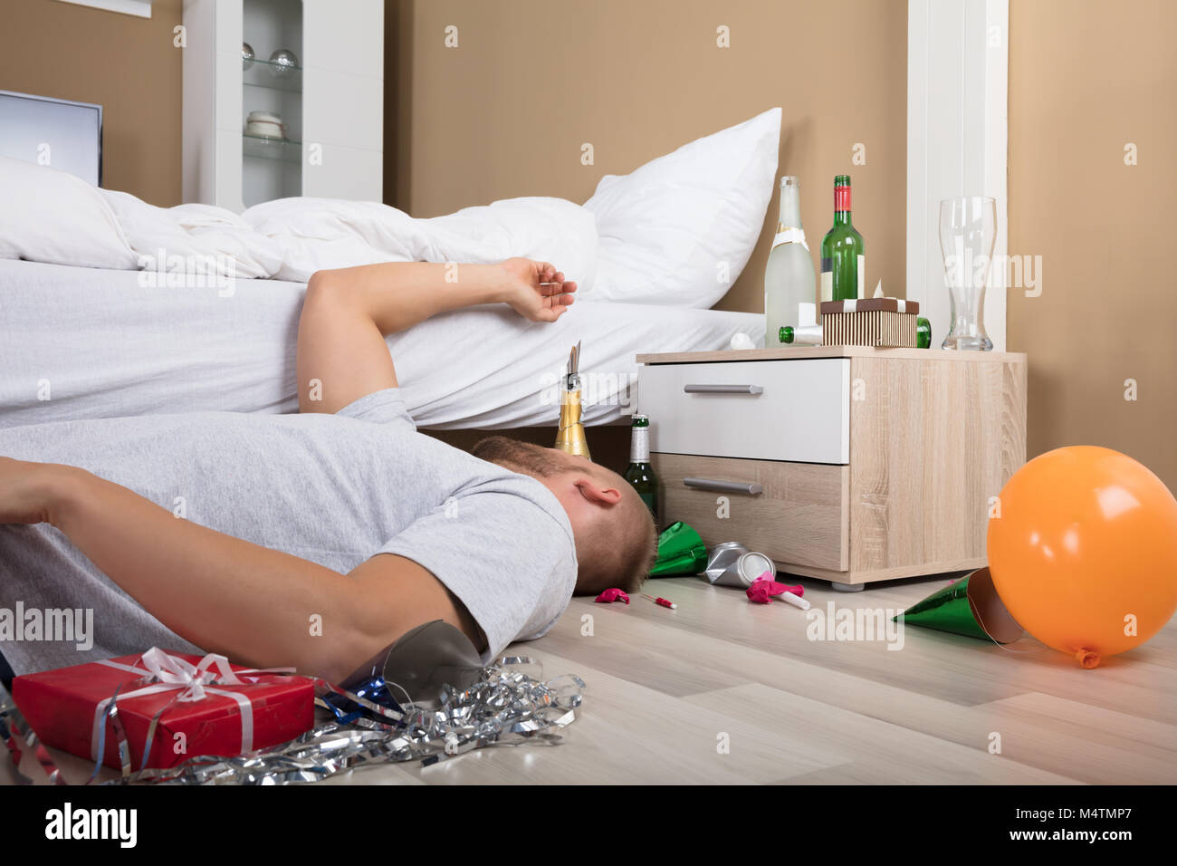 Man Sleeping On Messed Up Hardwood Floor With Beer Bottles On Nightstand Stock Photo