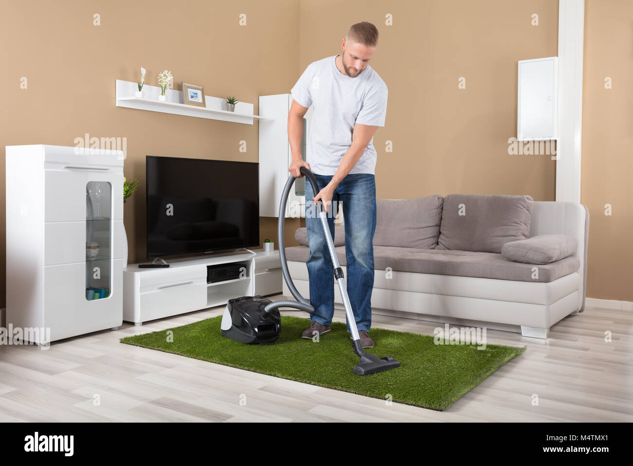 Young Man Cleaning Carpet With Vacuum Cleaner In Living Room Stock