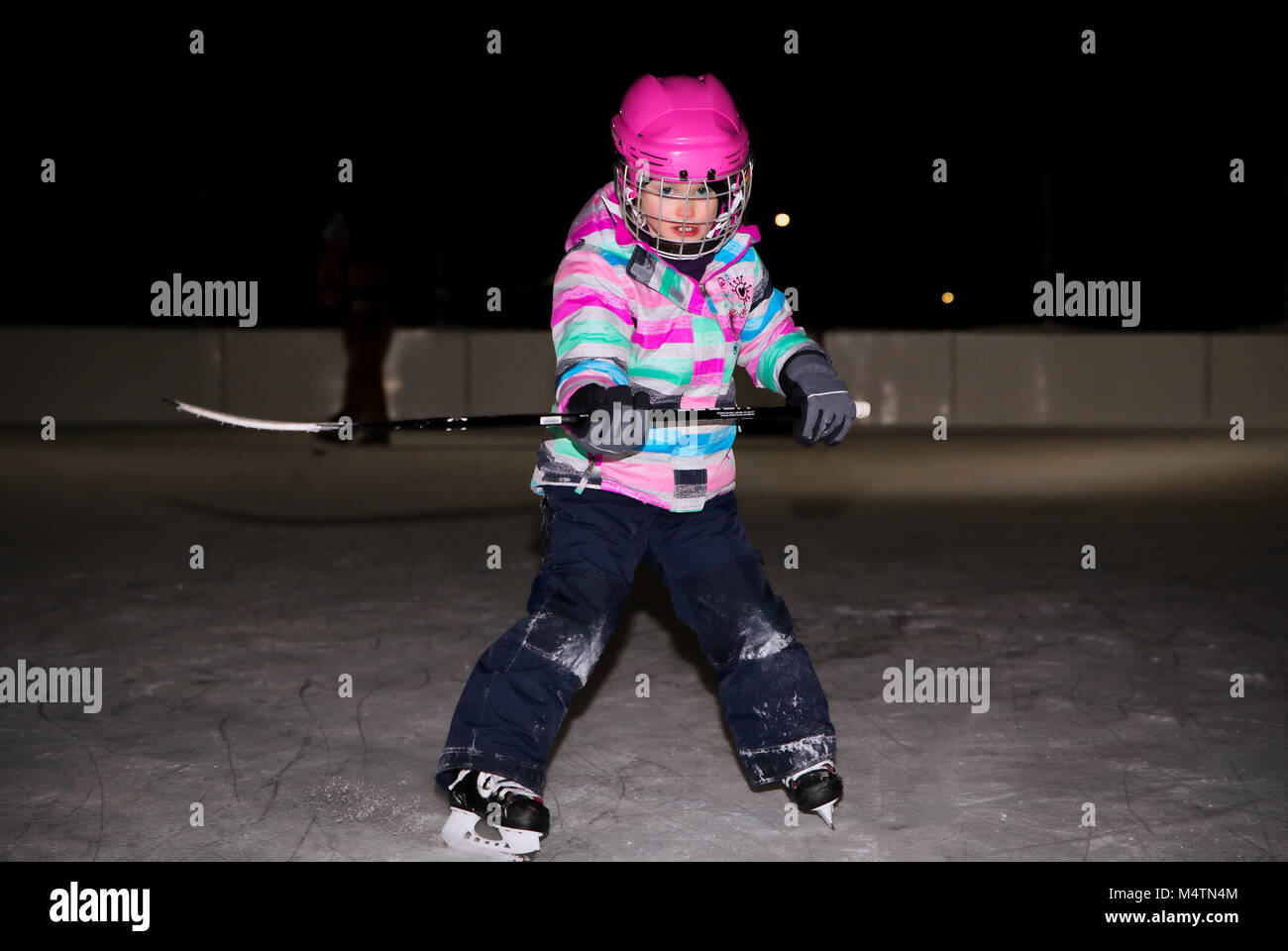 A five year old girl in hockey gear learning to stop with her skates on
