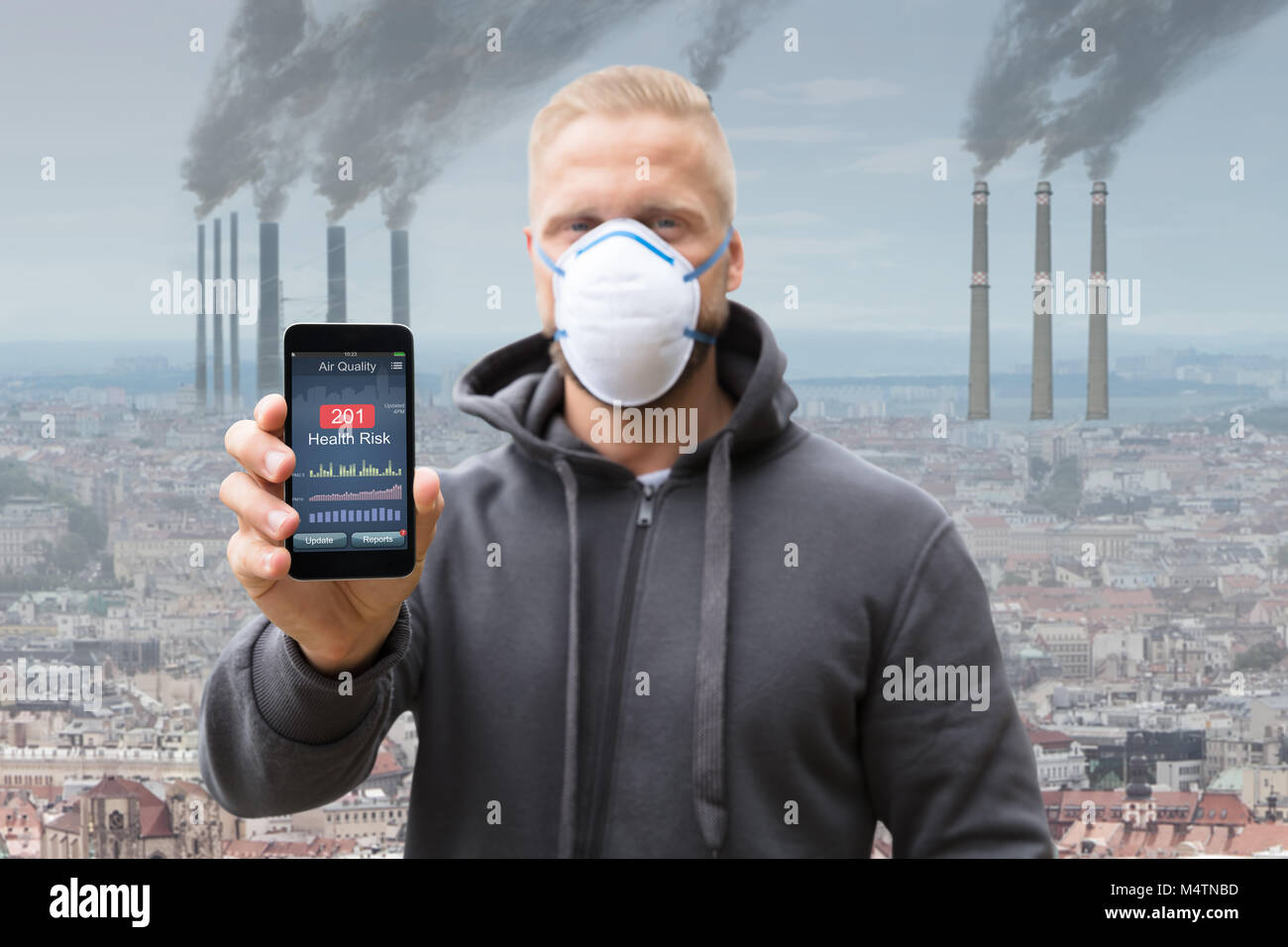 Man Showing Health Risk Rate On Cell Phone Against Smoke Emitting From Factory Chimneys Stock Photo