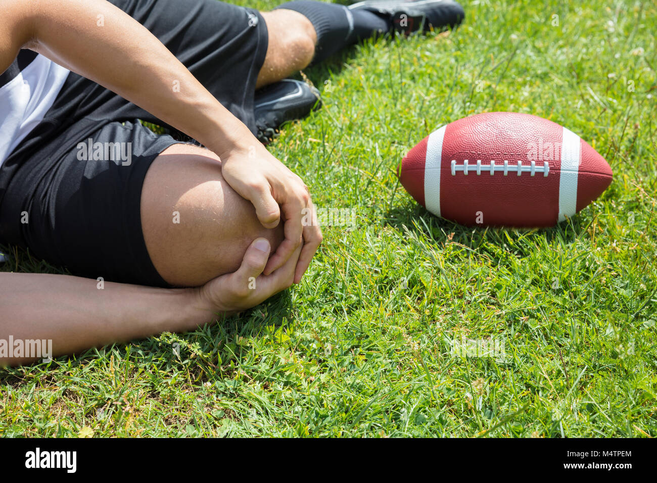 Closeup Of Male Rugby Player Suffering From Knee Injury Lying On Field