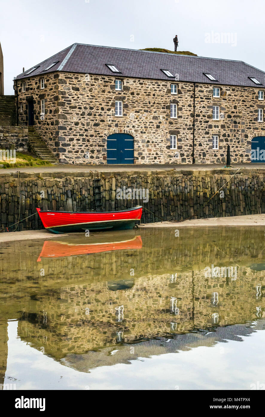 Small red rowing boat at low tide, picturesque harbour, Portsoy, Aberdeenshire, Scotland, UK, with water reflections and historic building Stock Photo