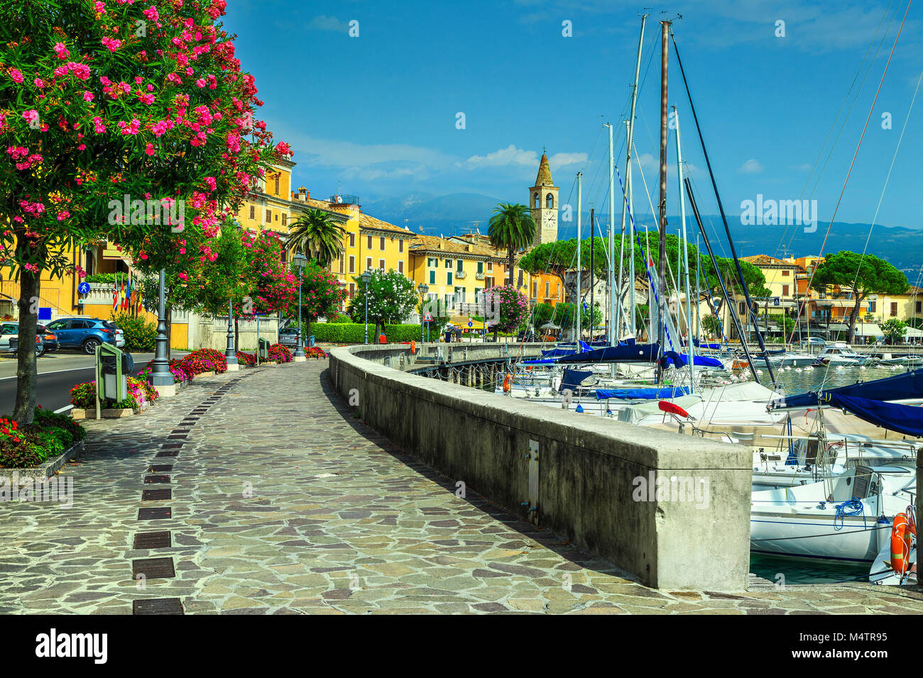 Stunning paved walkway with colorful Mediterranean flowers. Luxury yachts and boats in wonderful harbor of Toscolano-Maderno, lake Garda, Lombardy reg Stock Photo
