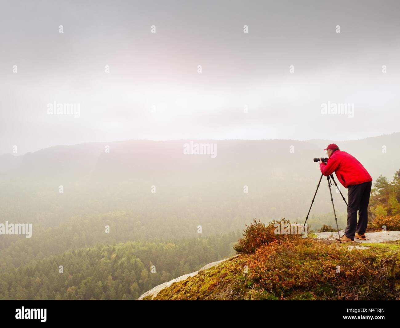 Professional photographer shooting. Artist stay  with tripod on summit and  takes pictures of autumnal coutryside. Misty landscape, cold sunrise in fa Stock Photo