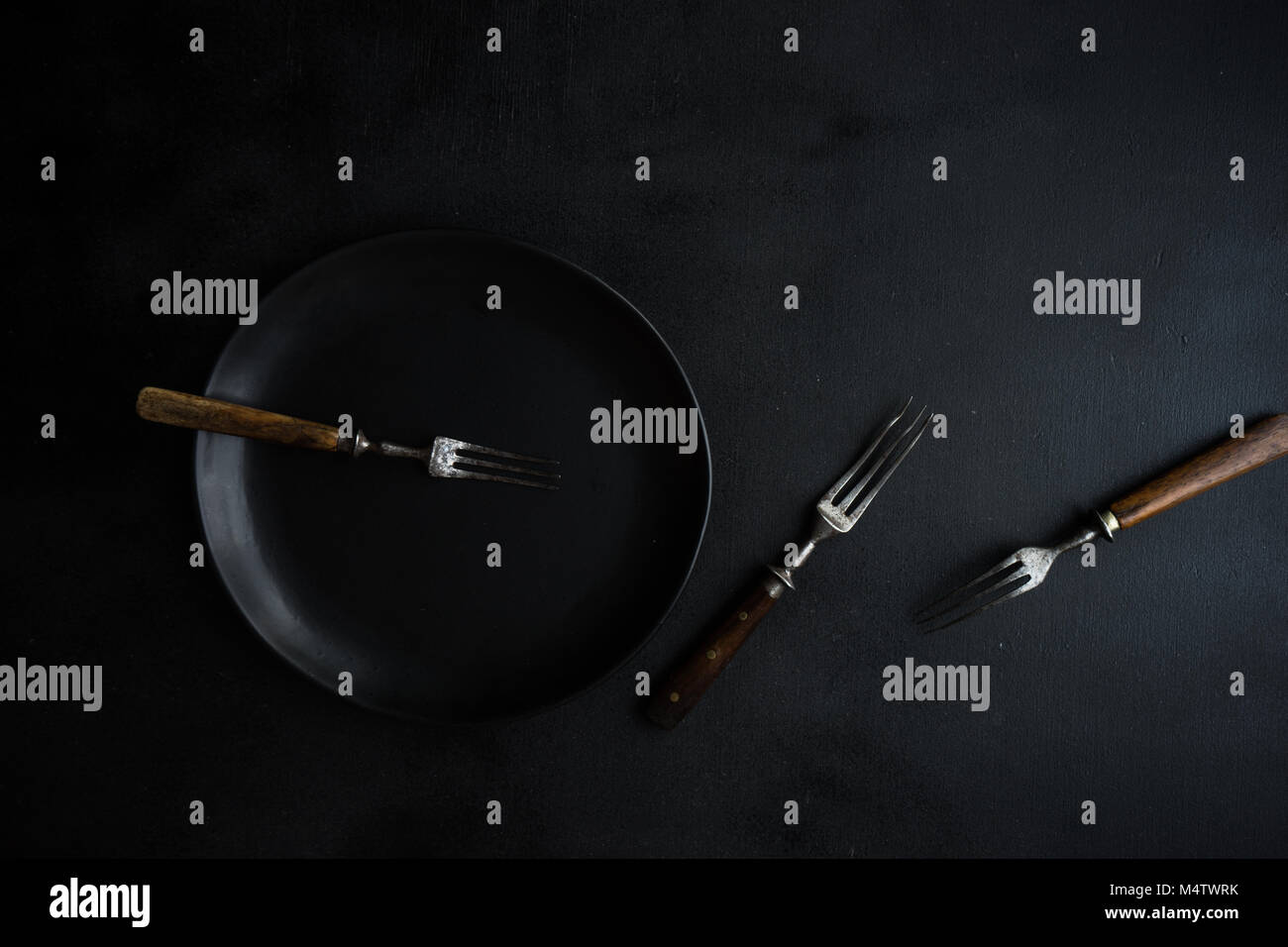 Dark table setting with black plate with silverware Stock Photo - Alamy