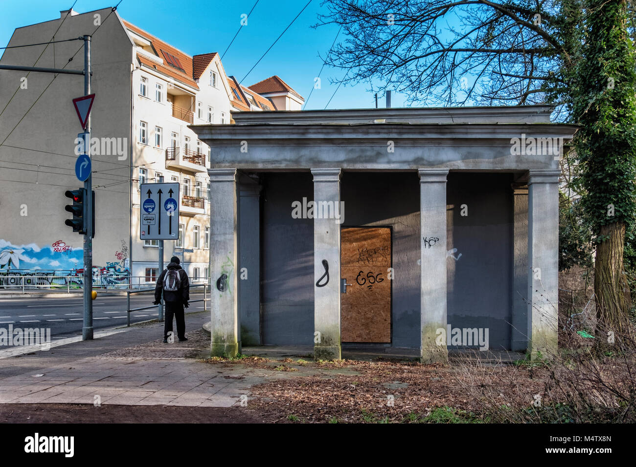 Bürgerpark Pankow Berlin.Old graffiti covered kiosk building with columns at edge of park with street view & man walking Stock Photo
