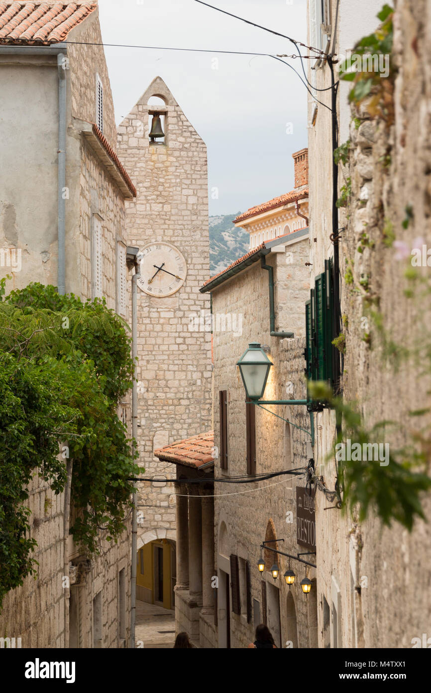 Narrow alleyway in Rab old town with clock / bell tower and houses built of white bricks and red roof tiles Stock Photo
