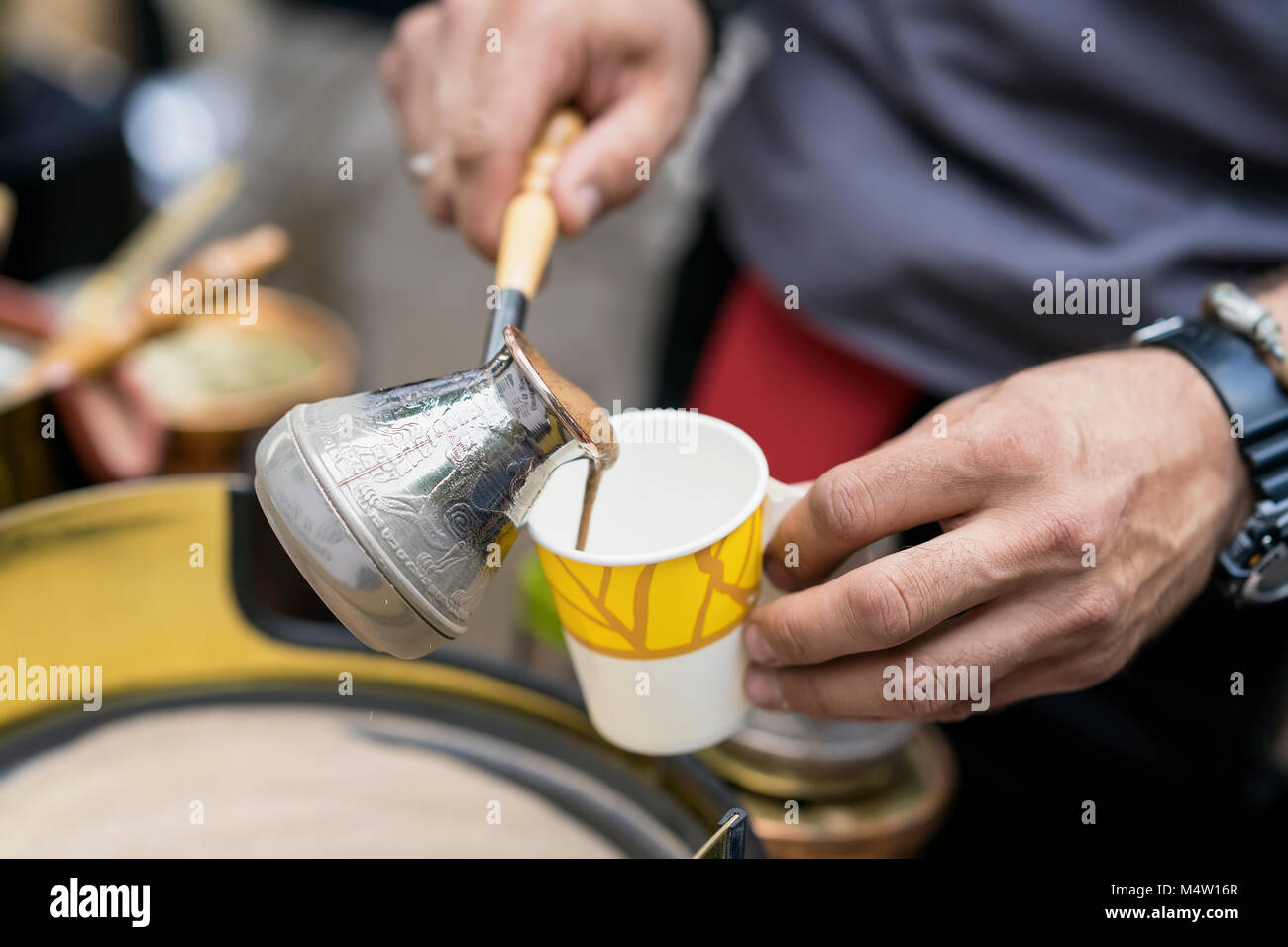 Close-up of hands of man making traditional turkish coffee in copper turk on hot sand and pours freshly prepared into disposable paper cup. Coffee preparation concept Stock Photo