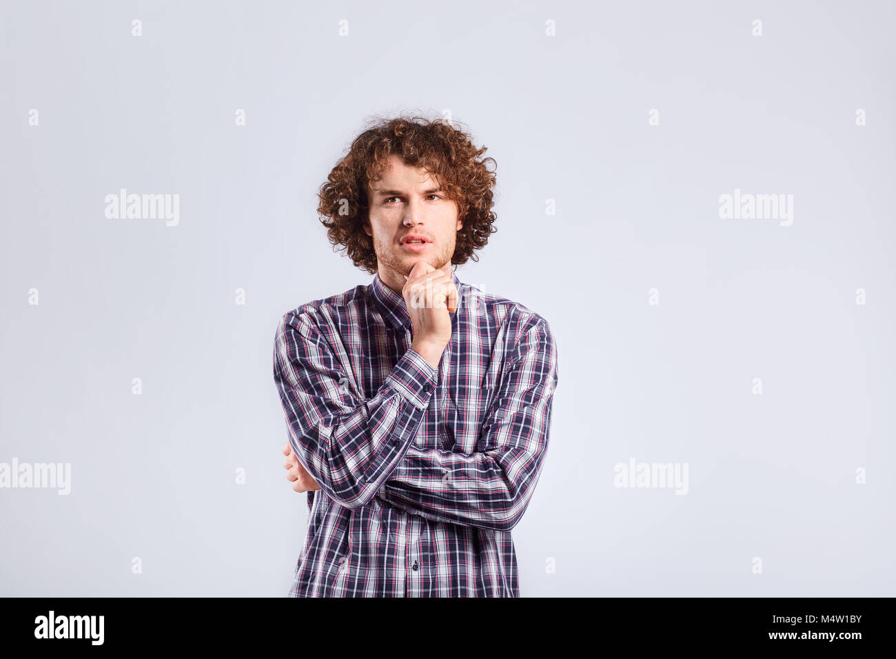 A young curly-haired man with a thoughtful emotion thinks lookin Stock Photo