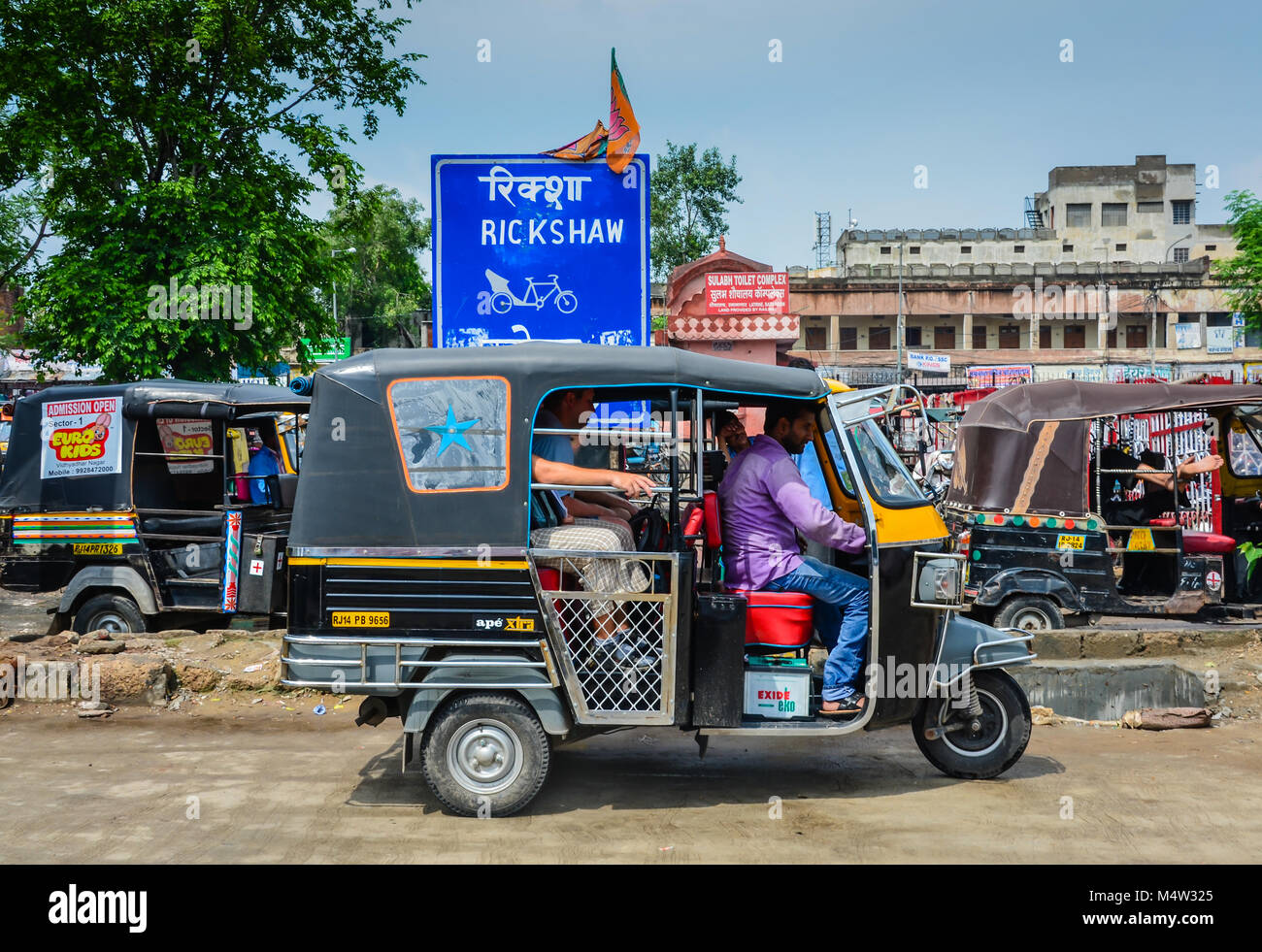 Auto rickshaw getting ready to leave stand of parked rickshaws awaiting fares. Stock Photo