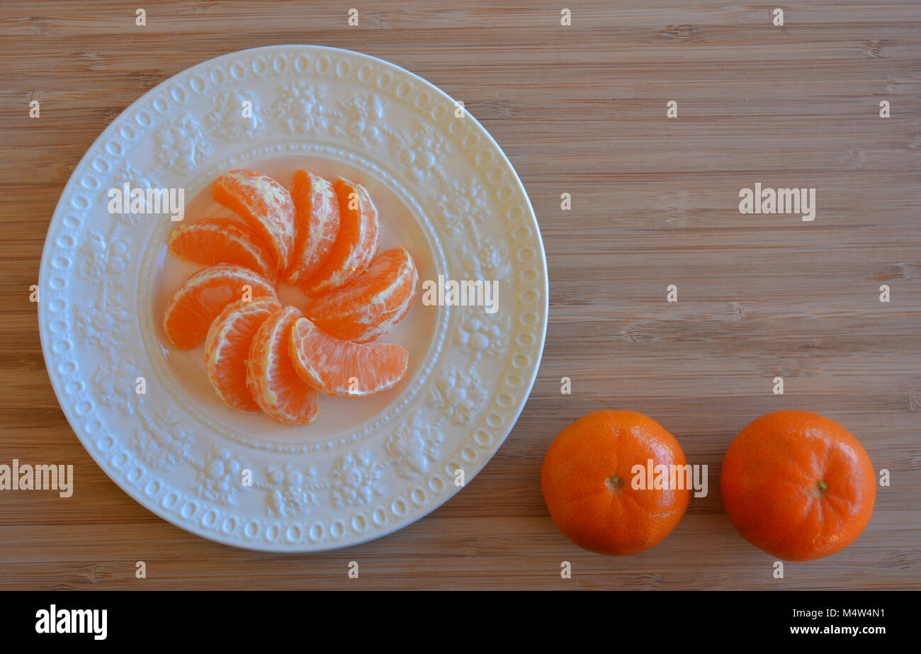 Mandarin oranges, one peeled and ready to eat on a plate, with copy