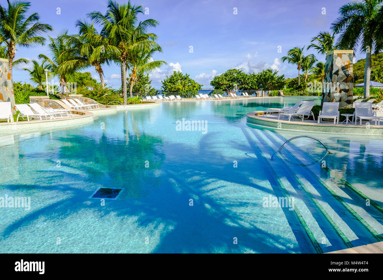 One of the Caribbean's largest, this huge pool fronts a white sand beach. The saltwater swimming pool is surrounded by white lounge chairs and tall pa Stock Photo