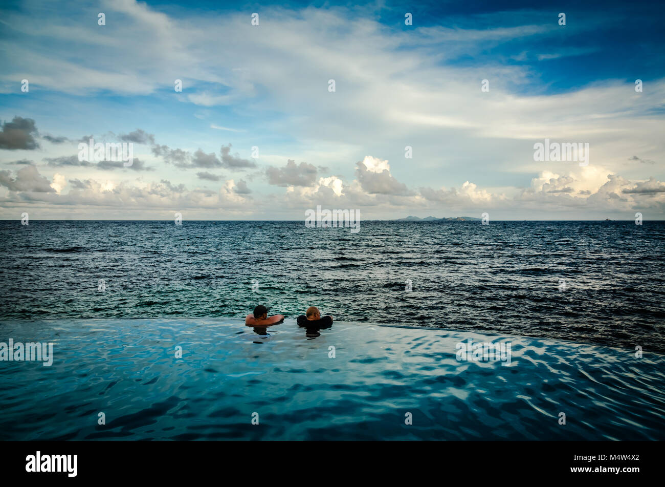 Two men hold onto the edge of an infinity pool overlooking the Caribbean Sea. Stock Photo
