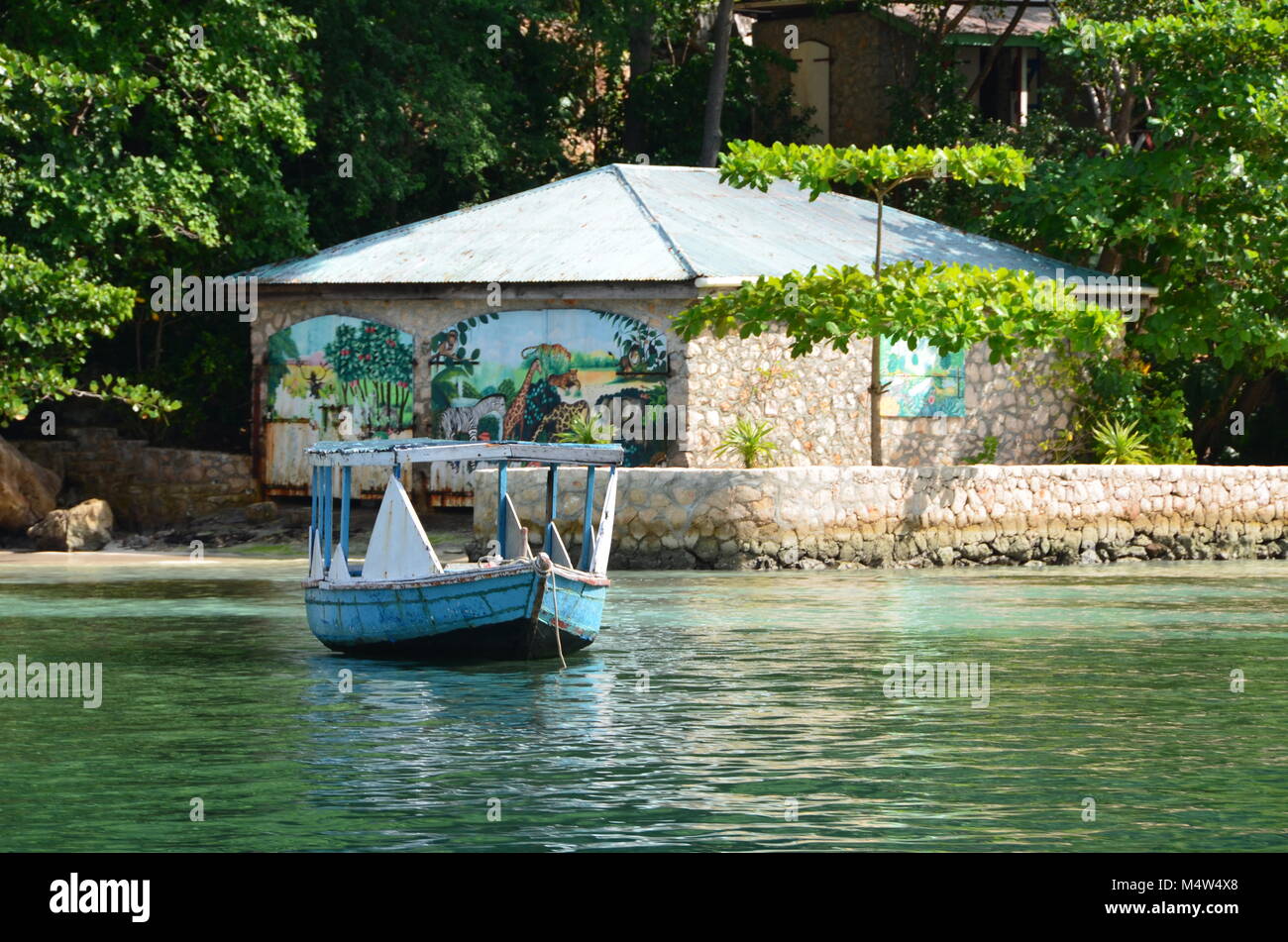 Labadee, Haiti. Haitian Village Experience shore excursion passes traditional wooden row boat and stone building with painted mural. Stock Photo