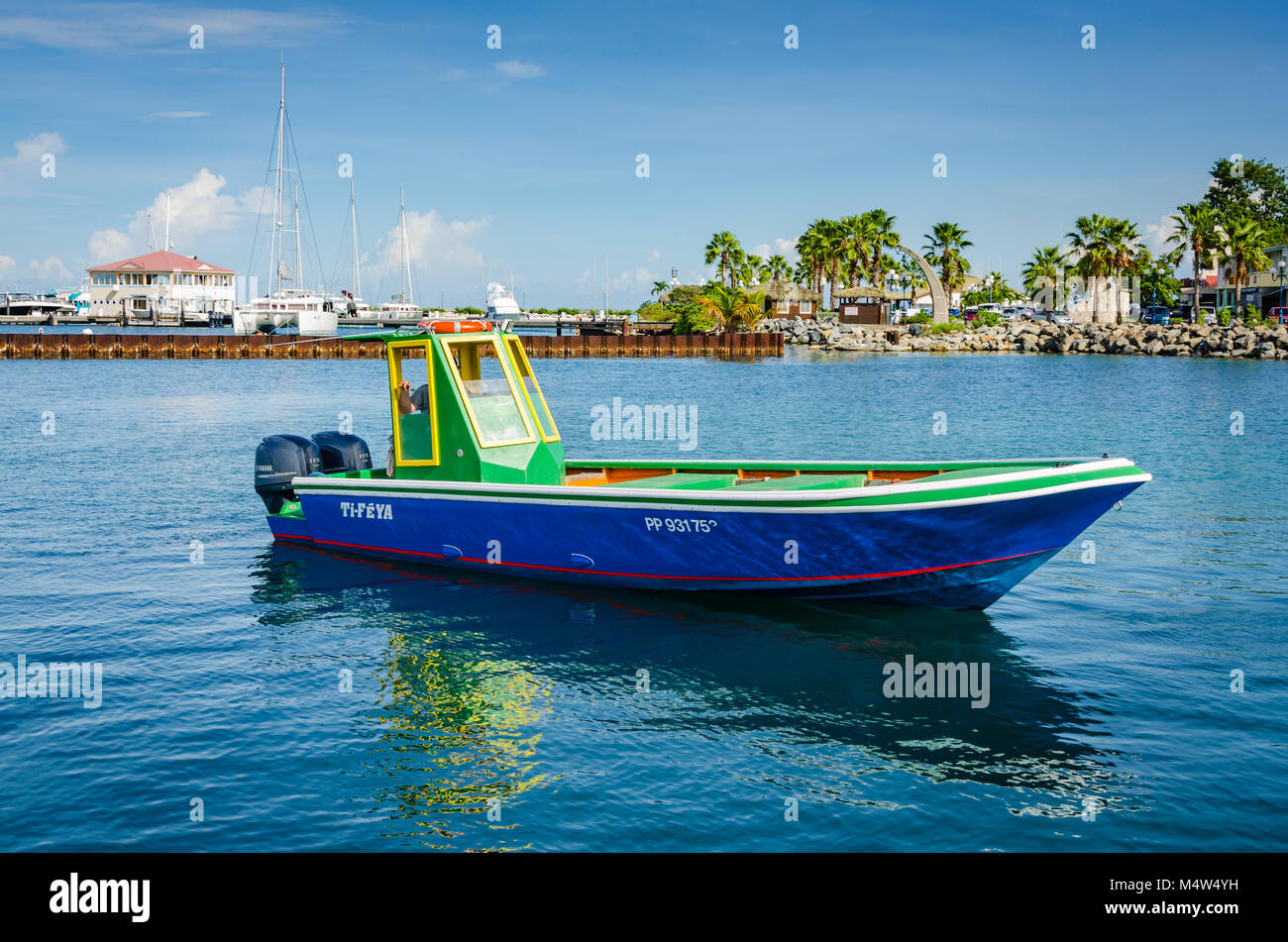 Vivid speedboat--painted in bright tropical hues of green, blue, and yellow--is reflected on turquoise ocean harbor of Gustavia in St. Barths. Stock Photo
