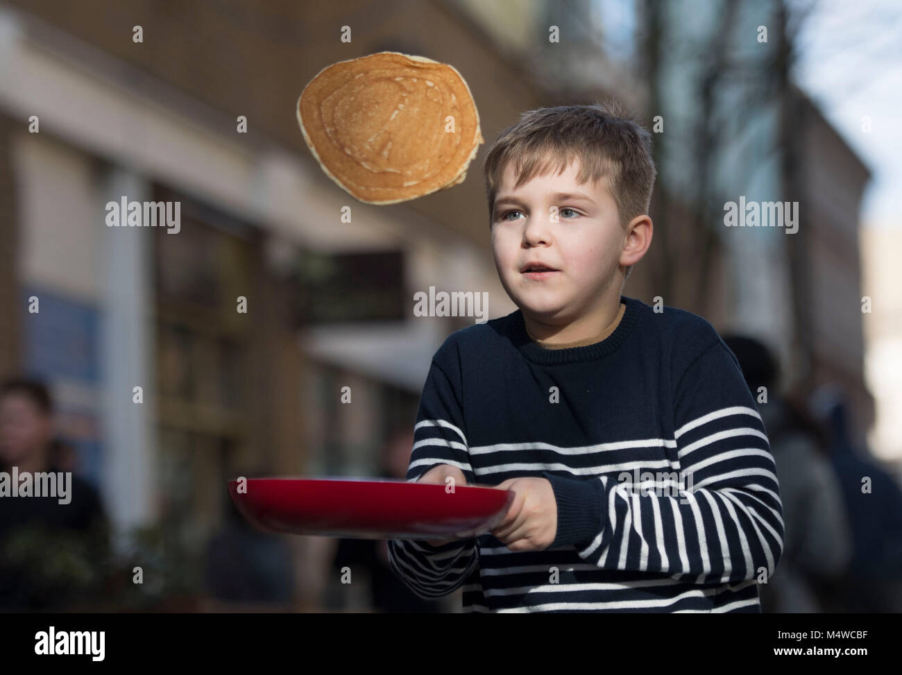 A boy flips pancakes using a frying pan on pancake day shrove tuesday