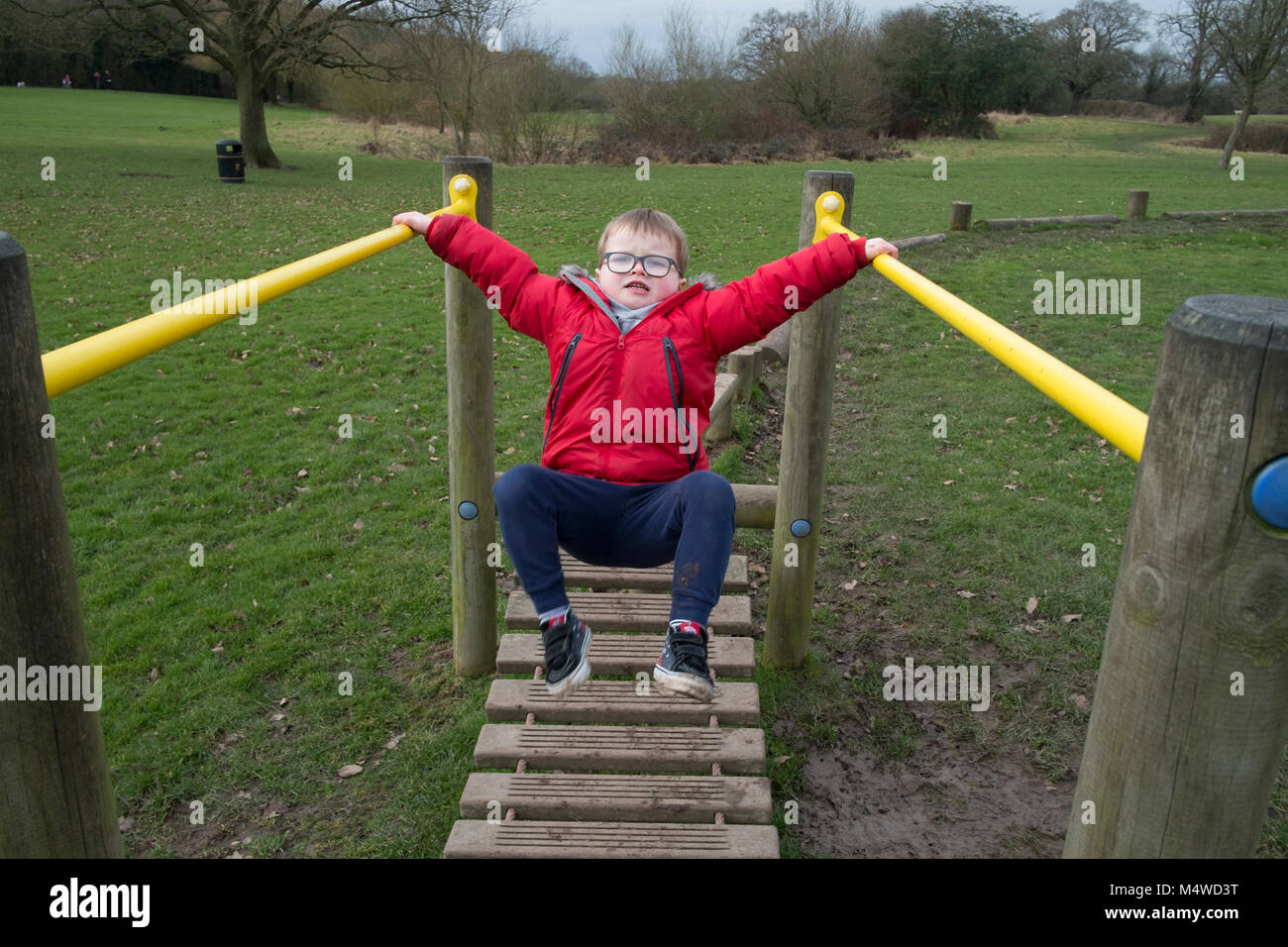 A young five year old boy playing on a set of parallel bars at an open