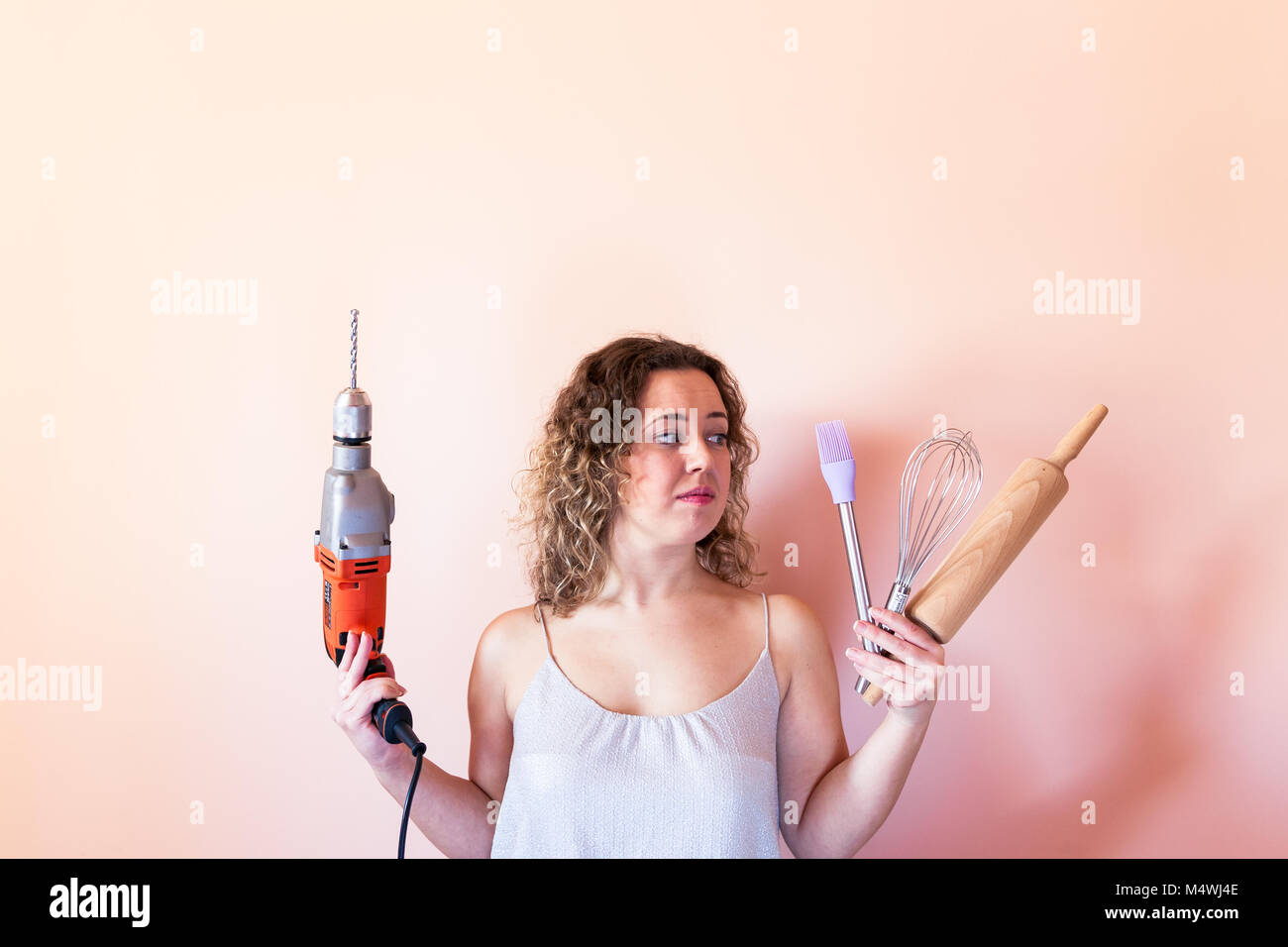 Beautiful curly woman holding man driller and kitchen tools. Gender equality, women's day concept. Stock Photo