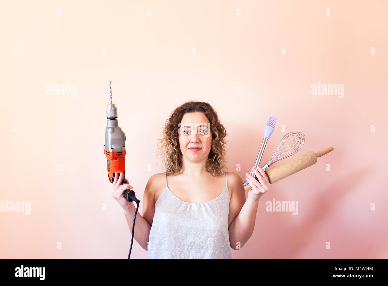 Beautiful curly woman holding man driller and kitchen tools. Gender equality, women's day concept. Stock Photo
