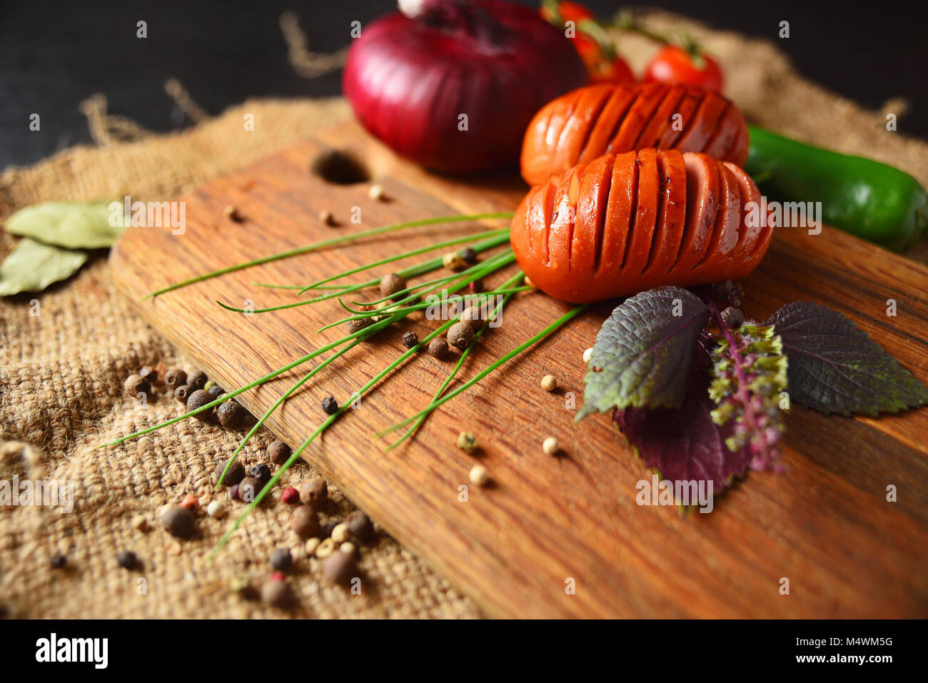 Grilled sausages on a wooden board with lettuce, basil, cherry tomatoes, onions and green peppers. Stock Photo