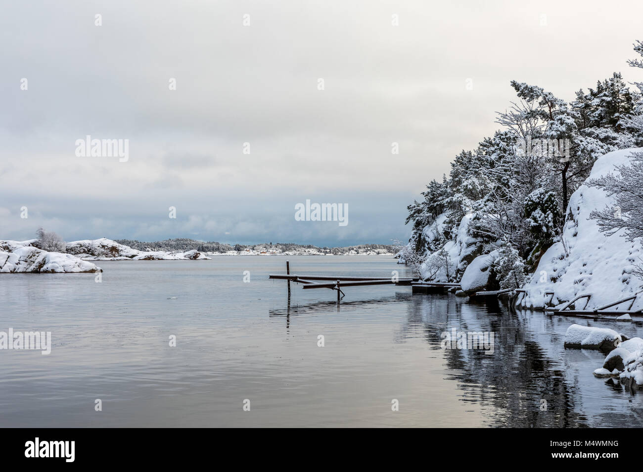 Reflections in the water. Beautiful winter day at Odderoya in Kristiansand, Norway. Trees covered in snow. Stock Photo