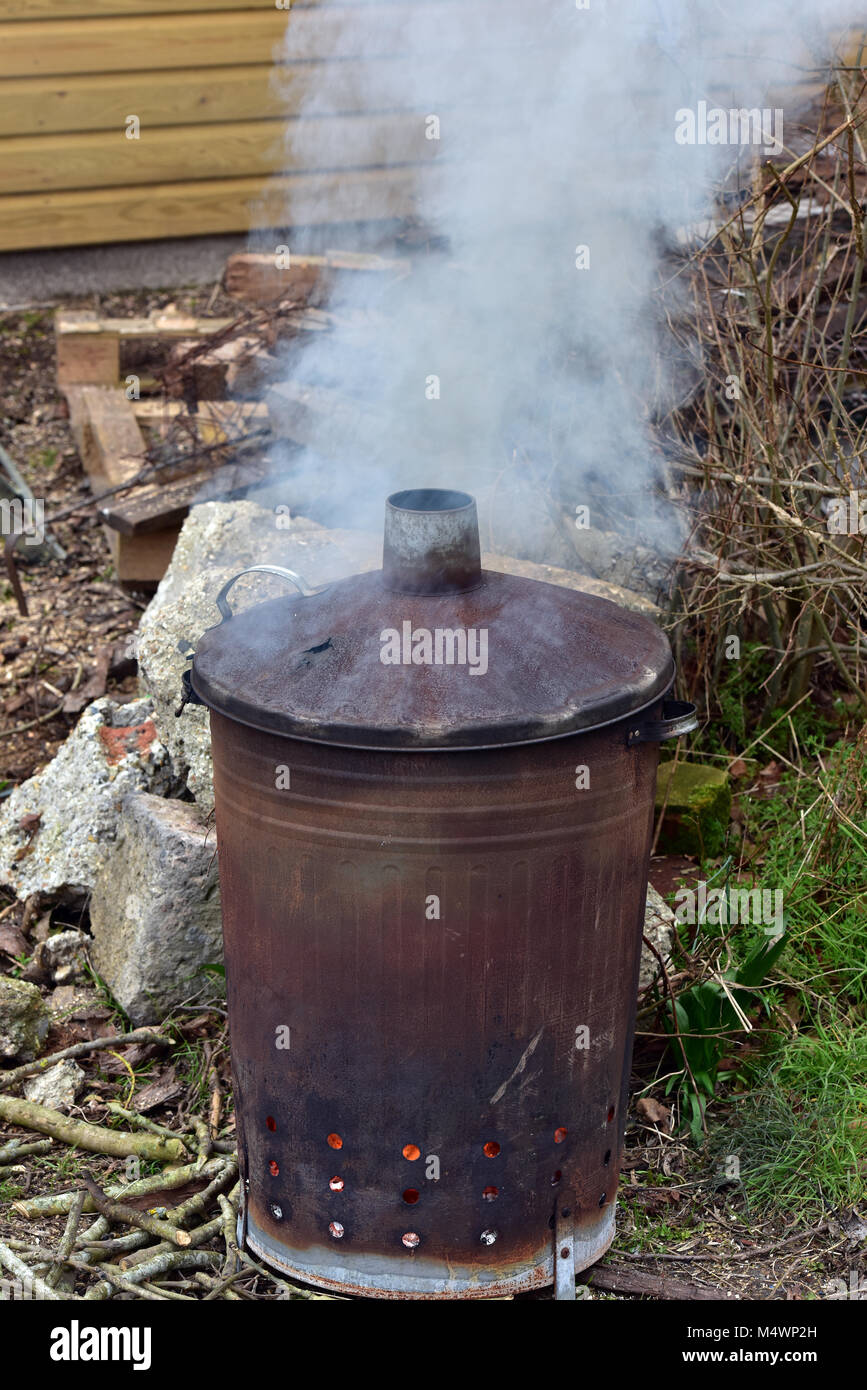 A garden bonfire or incinerator smoking burning gardening rubbish and waste. Fires in the garden getting rid of gardeners trash and cuttings. Dustbin. Stock Photo