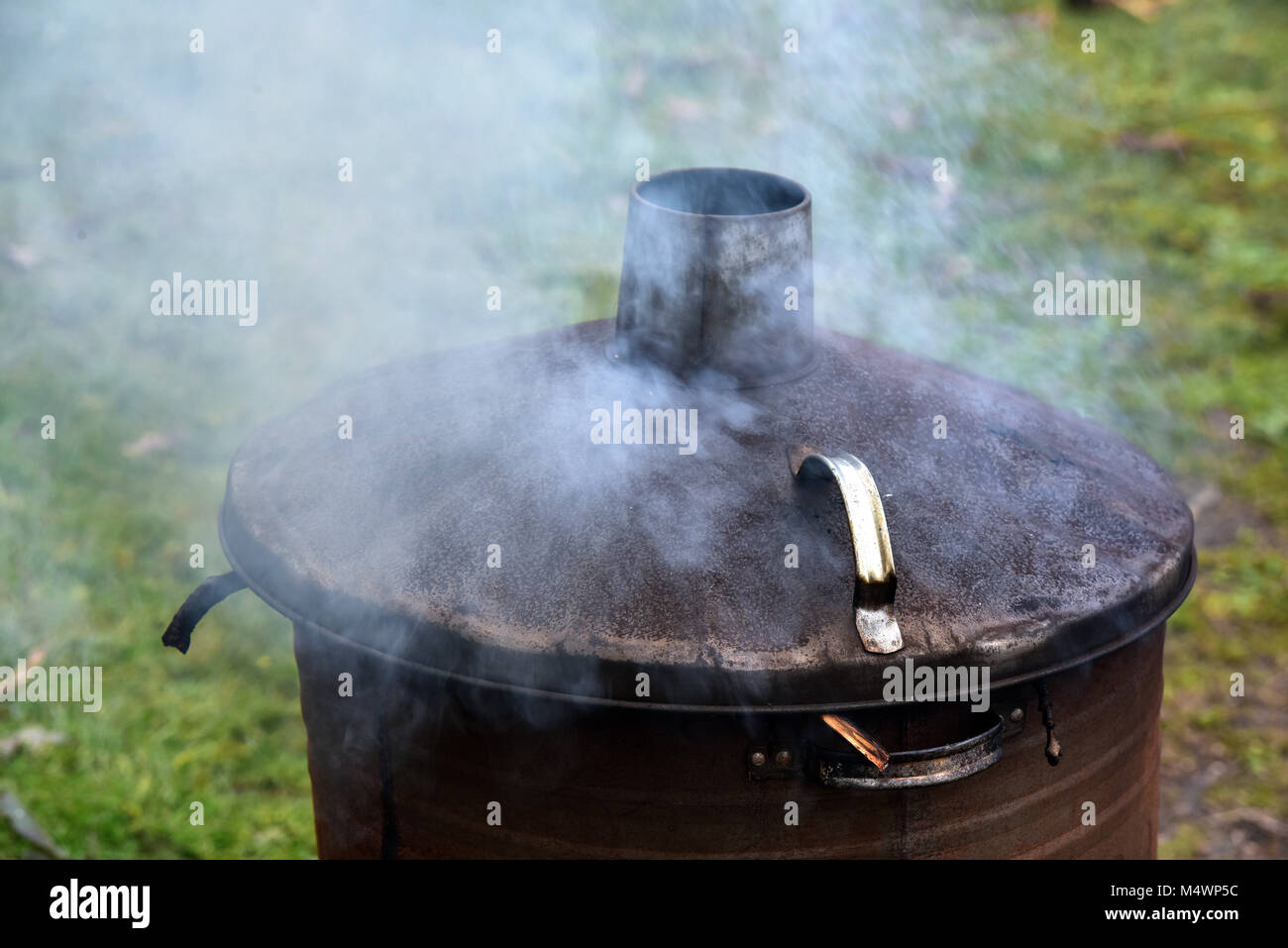 A garden incinerator or dustbin with a bonfire burning gardening wate in a galvanised metal bin with a lid smoking heavily neighbours from hell. Stock Photo